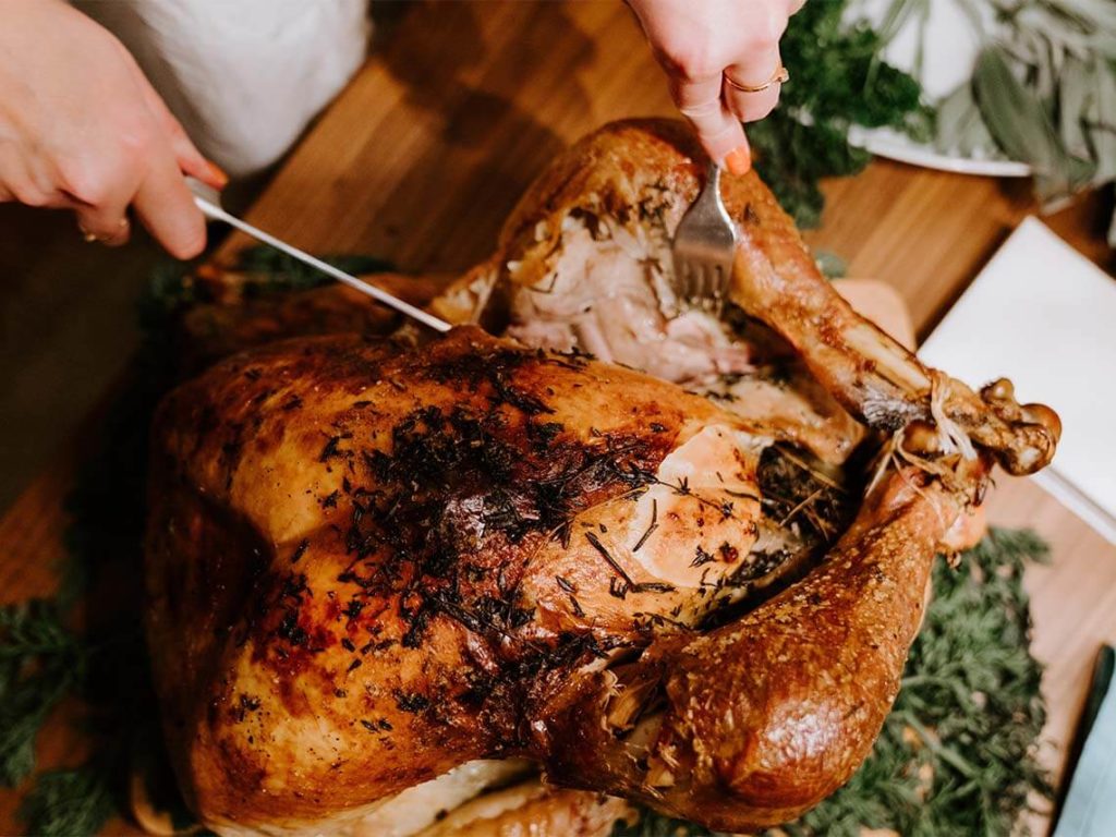 A woman is cutting the leg of her Thanksgiving turkey